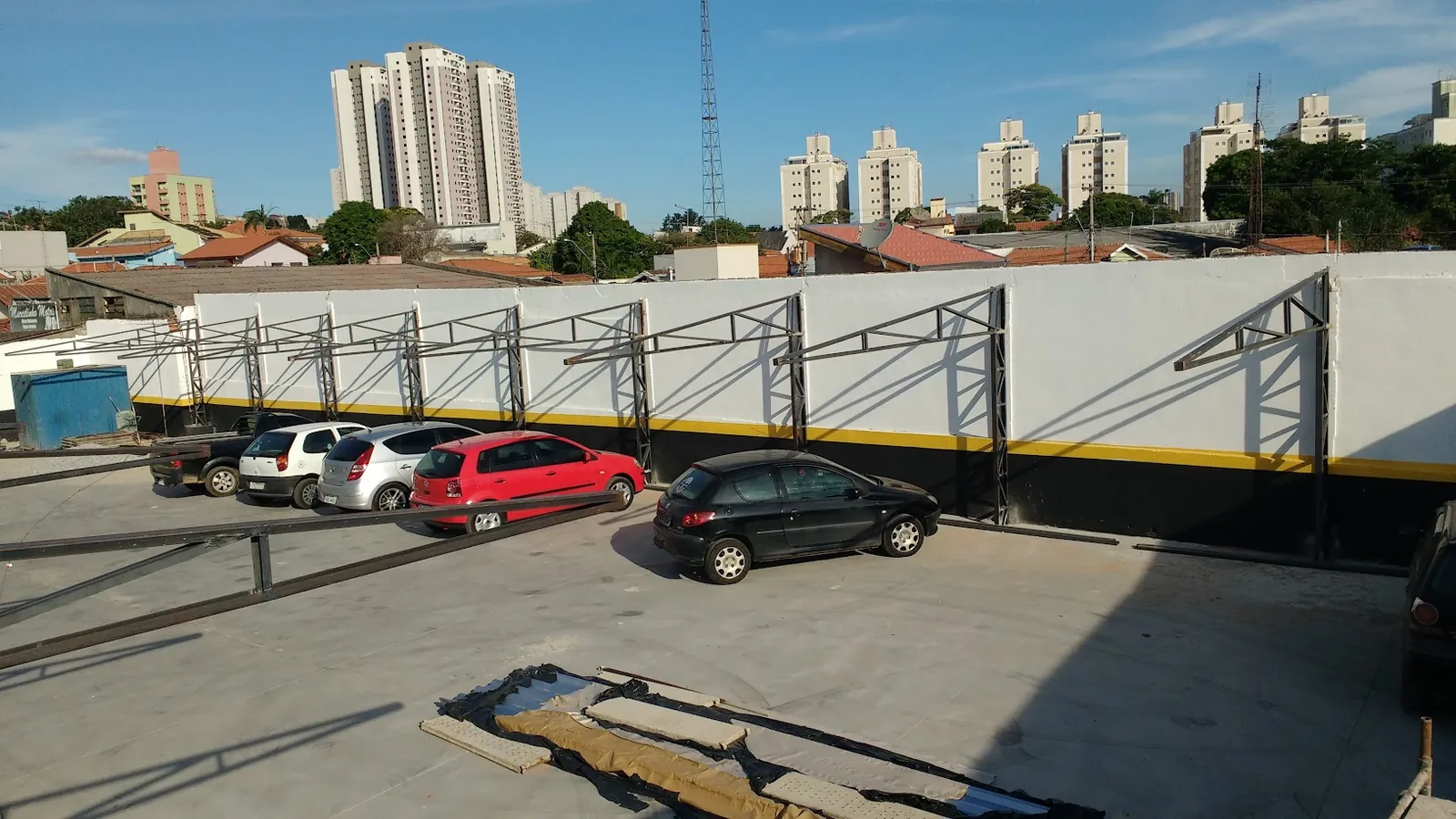 Pátio com piso de concreto e cobertura em estrutura metálica sendo montada junto ao muro